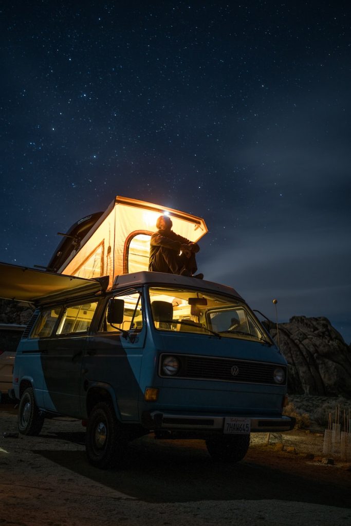 man sitting on top of blue van staring at sky during nighttime odour free